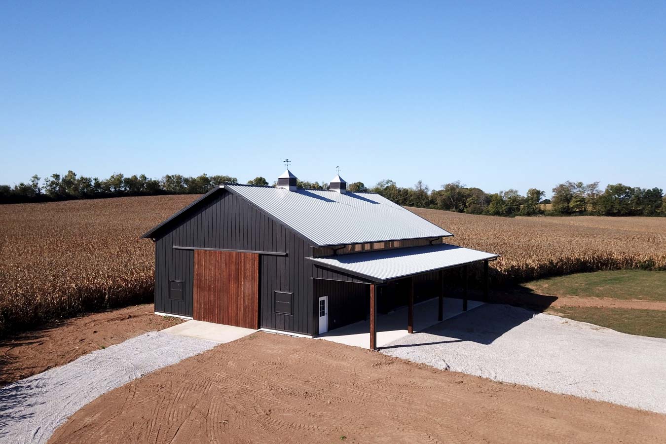 Project #41-3921 Aerial view of 40x64 post-frame pole barn with black siding, wood sliding doors, and lean-to in rural Kentucky field