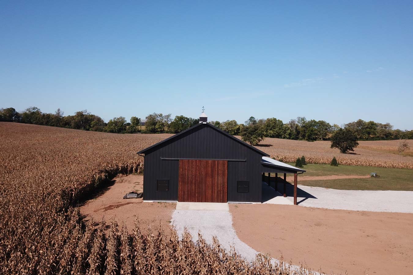 Front view of 40x64 pole barn with wood sliding doors, black metal siding, and gravel drive in farm setting