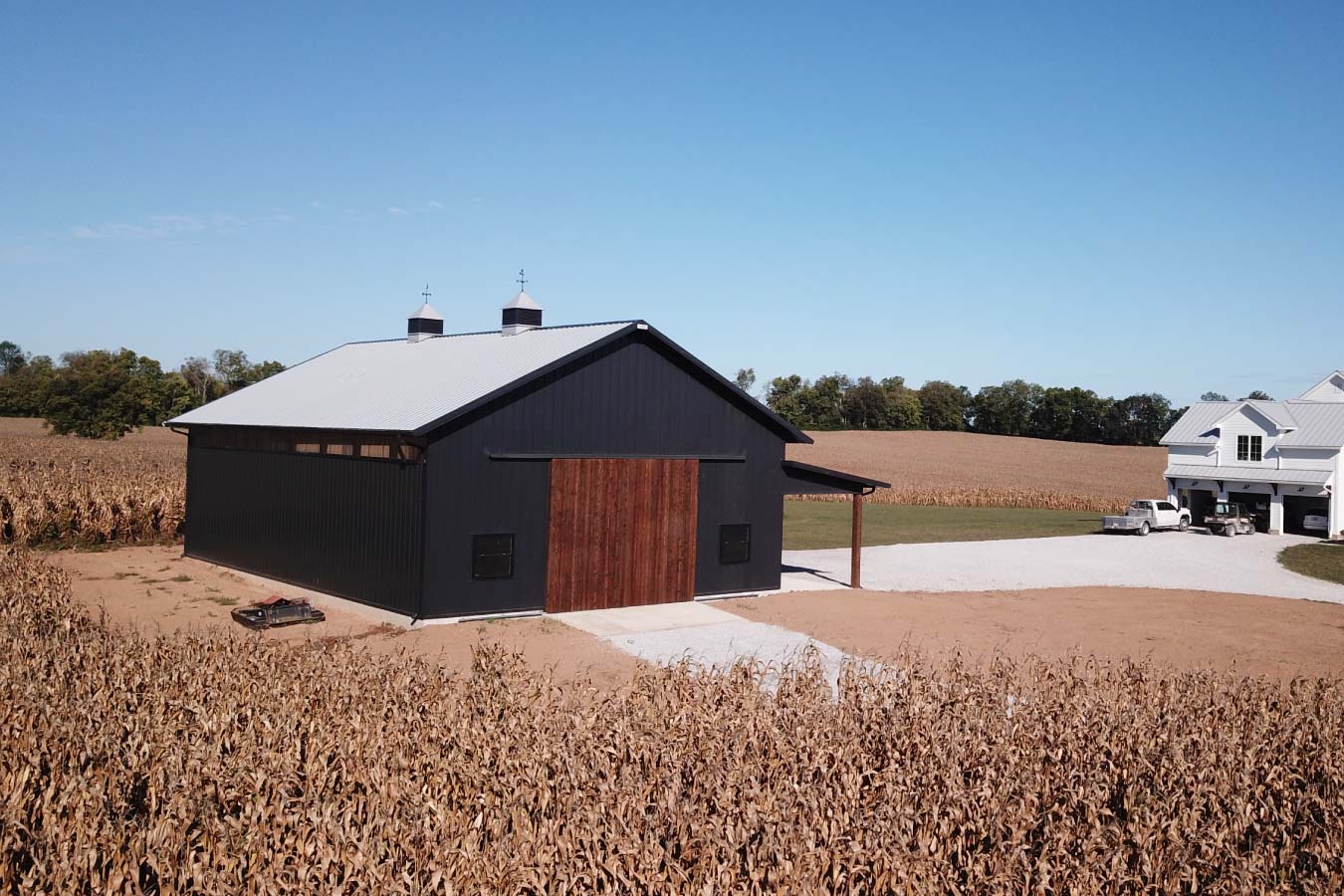 Side angle of black post-frame pole barn with wood doors and lean-to, set beside cornfield in rural Kentucky