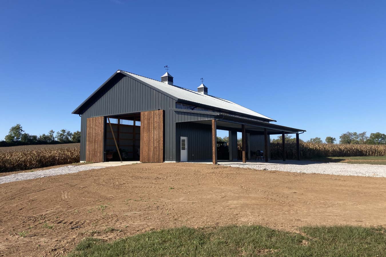 Exterior of pole barn with open wood sliding doors, black siding, and covered lean-to for equipment storage