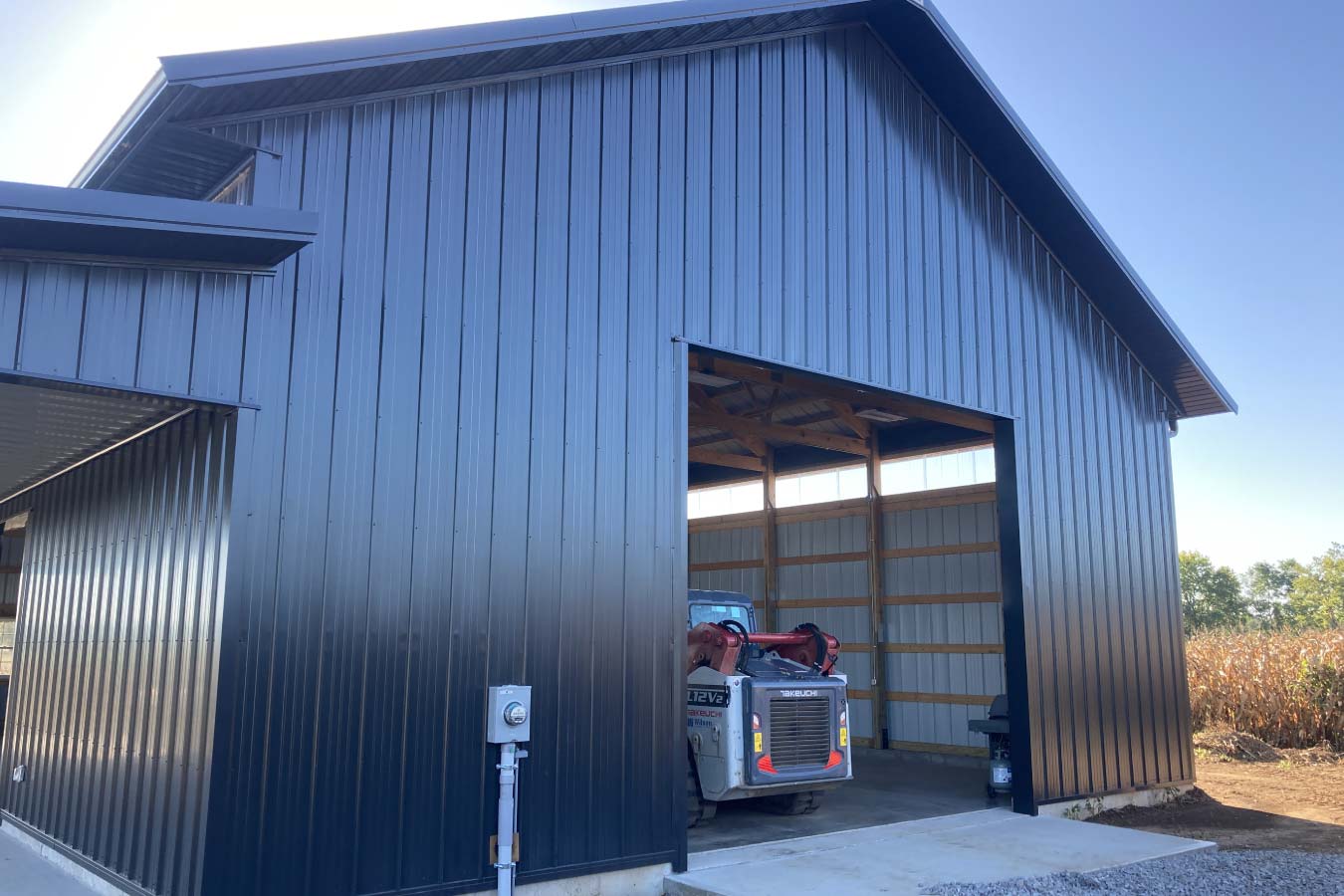 40x64 pole barn with black steel siding, oversized equipment opening, and heavy machinery storage