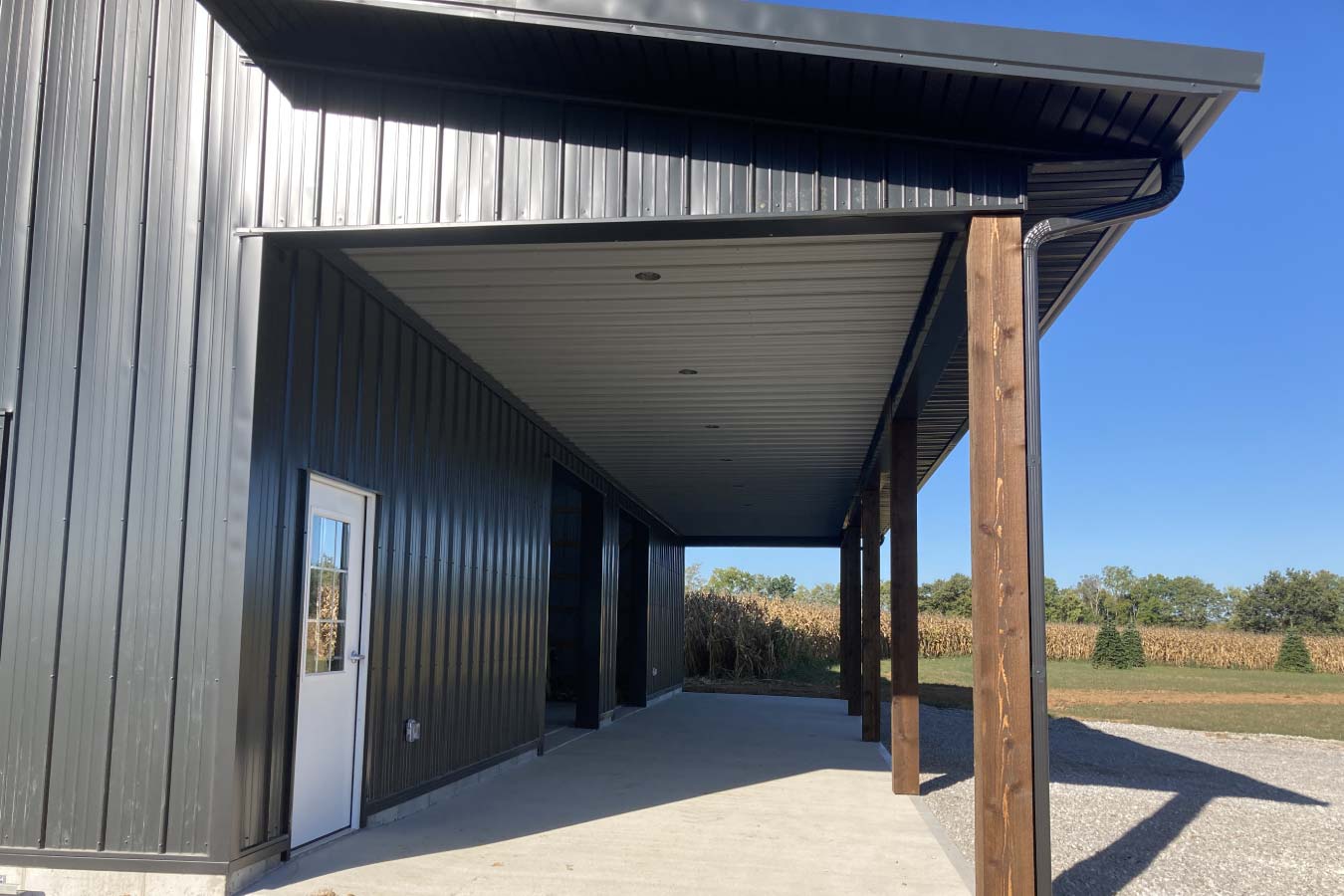 Covered lean-to area with wood posts, concrete floor, and recessed lighting on post-frame pole barn exterior