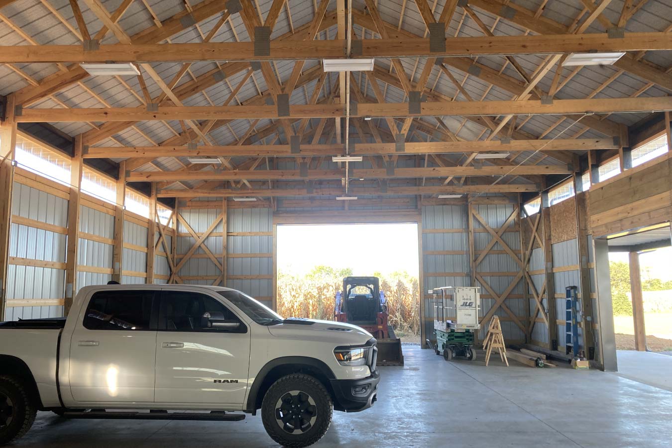 Interior of 40x64 pole barn with exposed wood trusses, vehicle storage, and open layout for equipment use