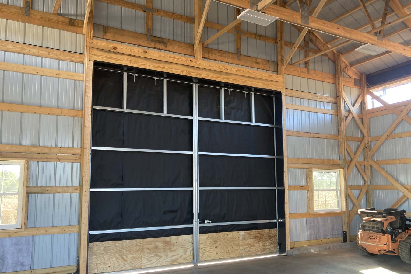 Interior detail of post-frame structure with large sliding door system, wood framing, and equipment storage space