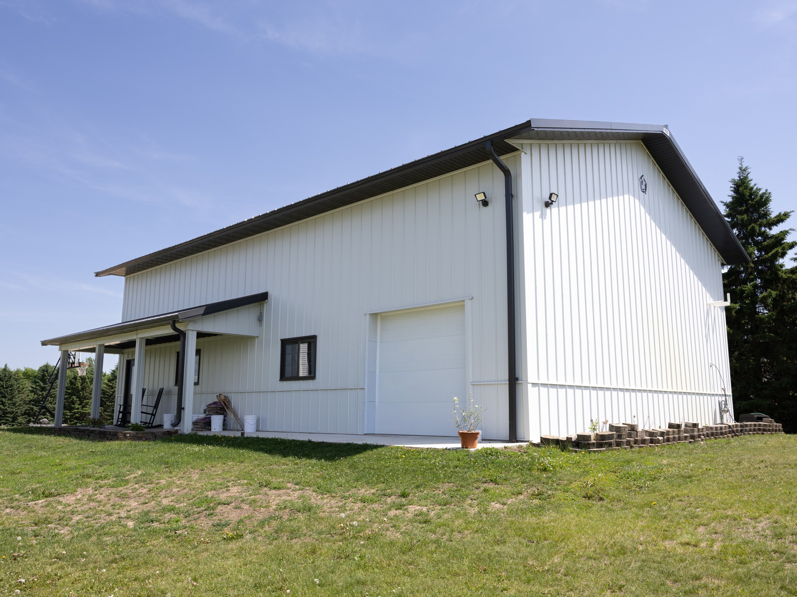 Side view of a 36x50 pole barn storage building with white steel siding, dark metal roof and covered porch
