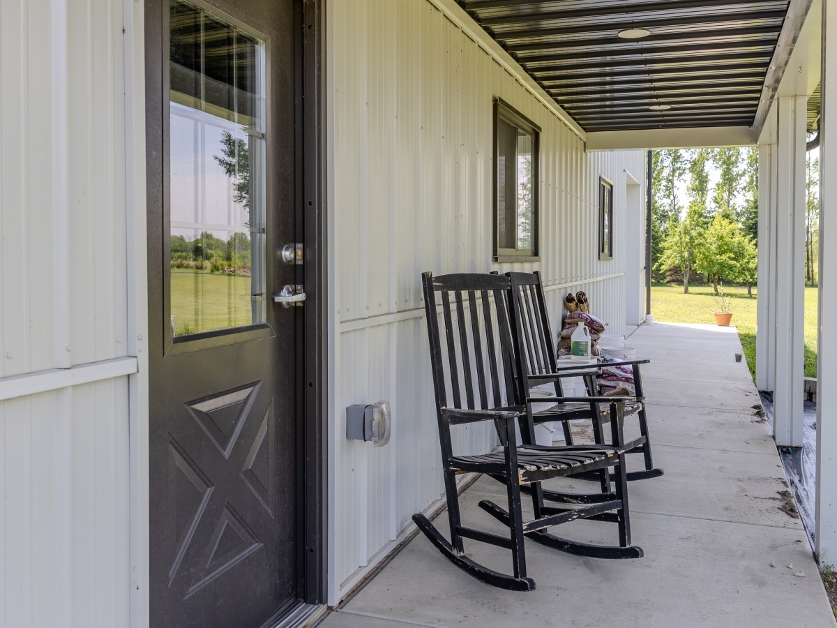 Covered porch on a pole barn garage with recessed ceiling lights, black walk door and windows