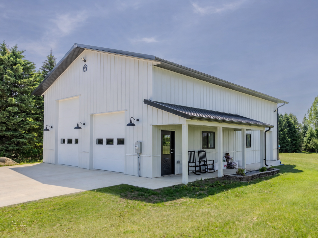 Residential pole barn garage in Jordan, Minnesota with white steel siding, black roof, covered porch and overhead doors
